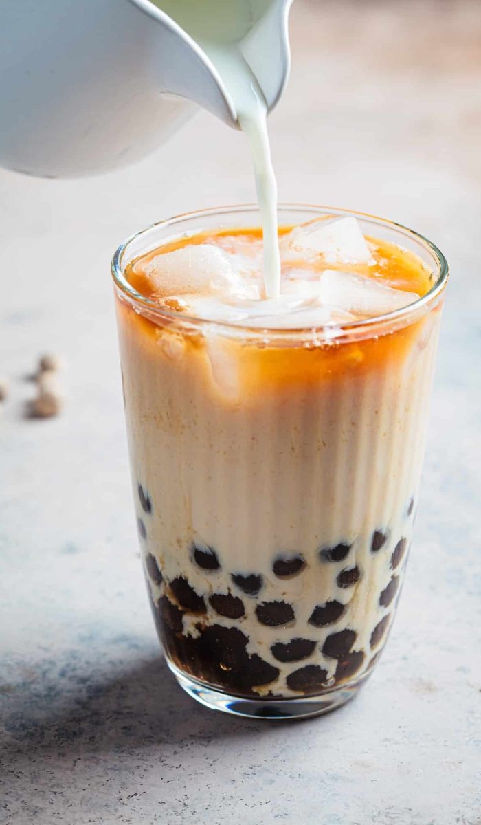 Milk bubble tea with tapioca pearls in glass, gray background.